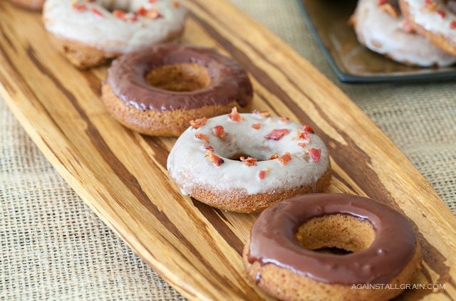 A display of baked pumpkin spiced doughnuts some with chocolate frosting and others with maple vanilla frosting with bacon sprinkles.