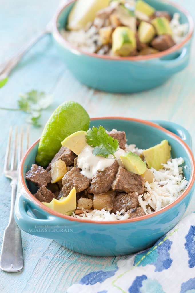 Crockpot Mexican Stew served over cauliflower rice and a side of fresh avocado. Served in a blue bowl on a light blue wooden table.