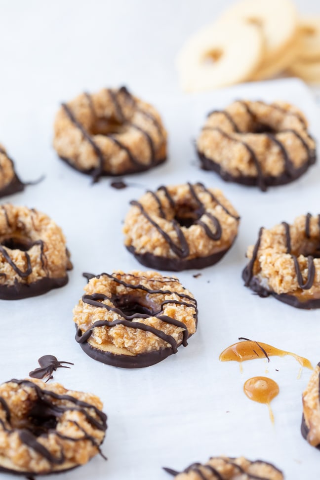 Up close view of samoa cookies with chocolate drizzle and caramel on a white surface with shortbread cookies in the background