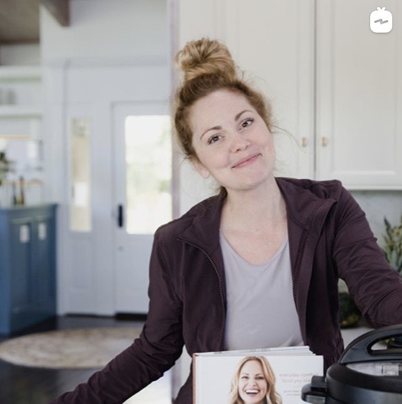 woman smiling at camera with her cookbook and instant pot in her home kitchen