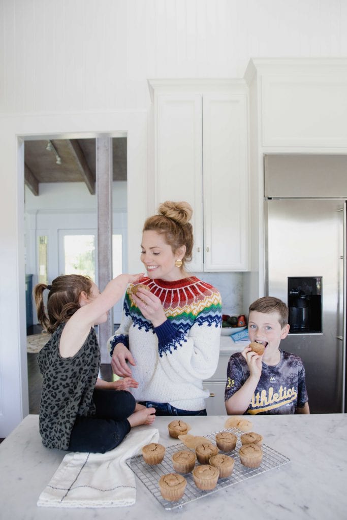 Woman and children in home kitchen enjoying freshly made muffins that are cooling on the counter on a wire rack