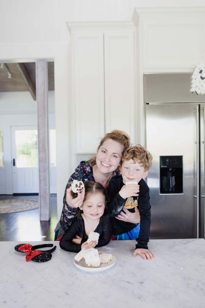 woman smiles at camera embracing two children while they all hold rice crispy halloween treats