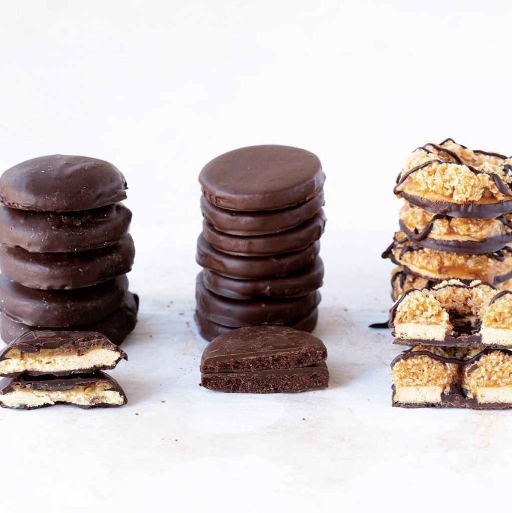 variety of cookies with chocolate (tagalong, thin mint and samoa) displayed in individual stacks on a white surface