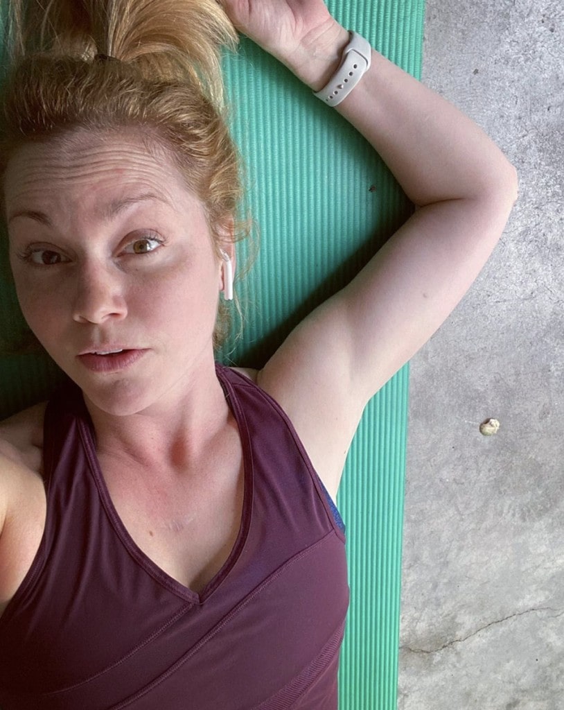 woman lays exhausted after a workout on a teal yoga mat wearing a purple tank