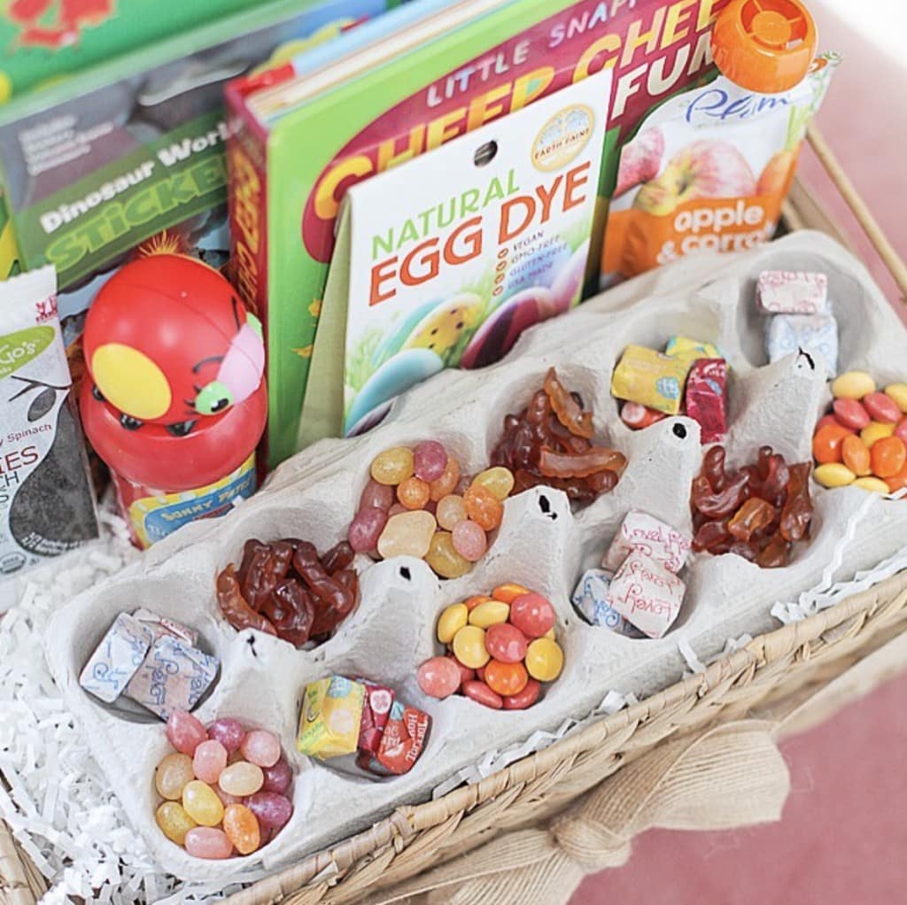 variety of Easter treats such as candy, egg dye, and books in tan weaved Easter basket