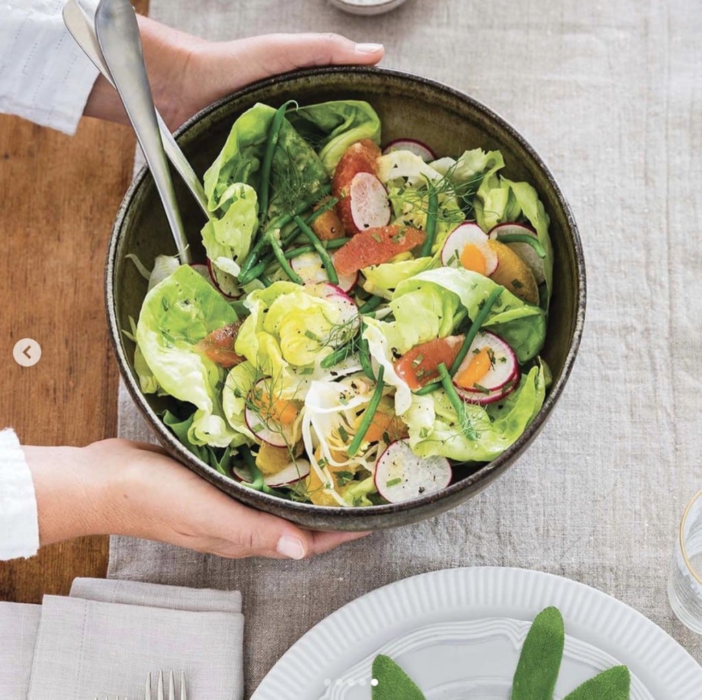 hands hold a bowl of mixed salad over table with settings