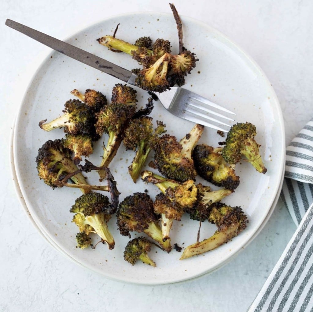 roasted broccoli on a white plate with a silver spoon on a white counter