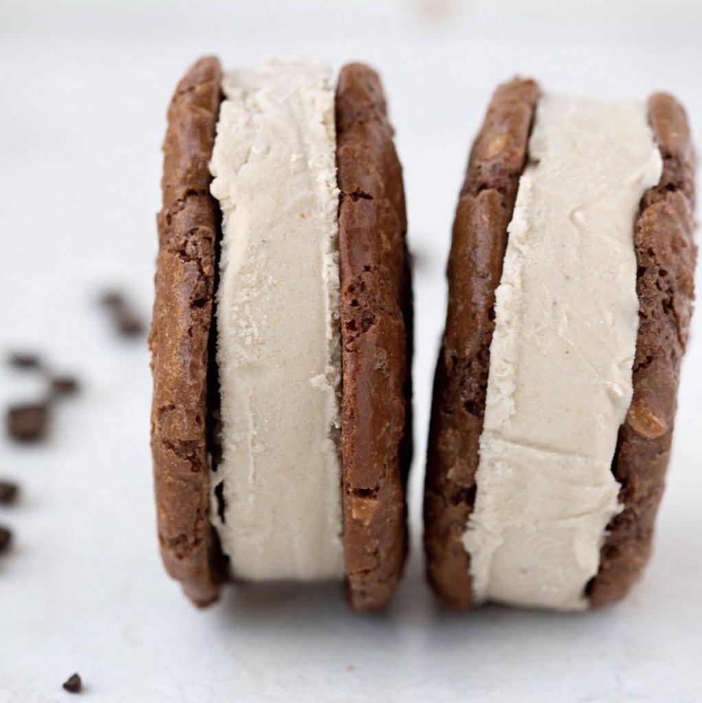 Two round ice cream sandwiches, made of a chocolate cookie and coffee ice cream, stand side by side on a white counter