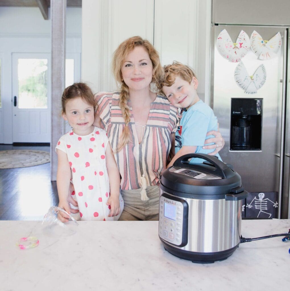 Woman embraces smiling young children in home kitchen standing in front of an Instant Pot