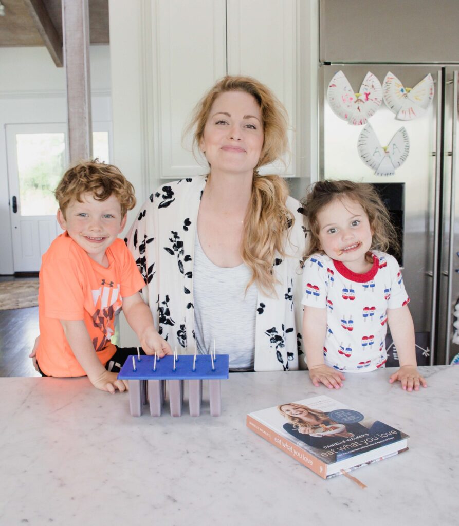Mother and two children stand in home kitchen in front of freshly made fudge popsicles in mold and copy of Eat What You Love cookbook