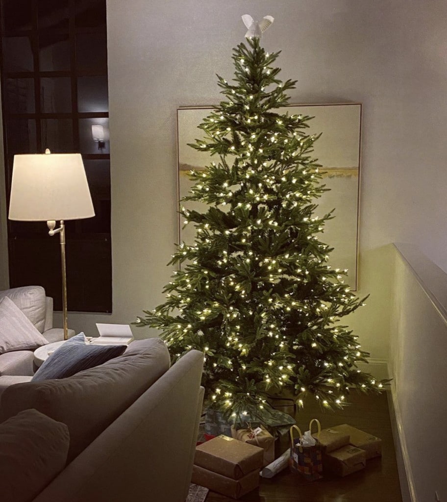 Lit up Christmas tree in living room corner with wrapped gifts underneath