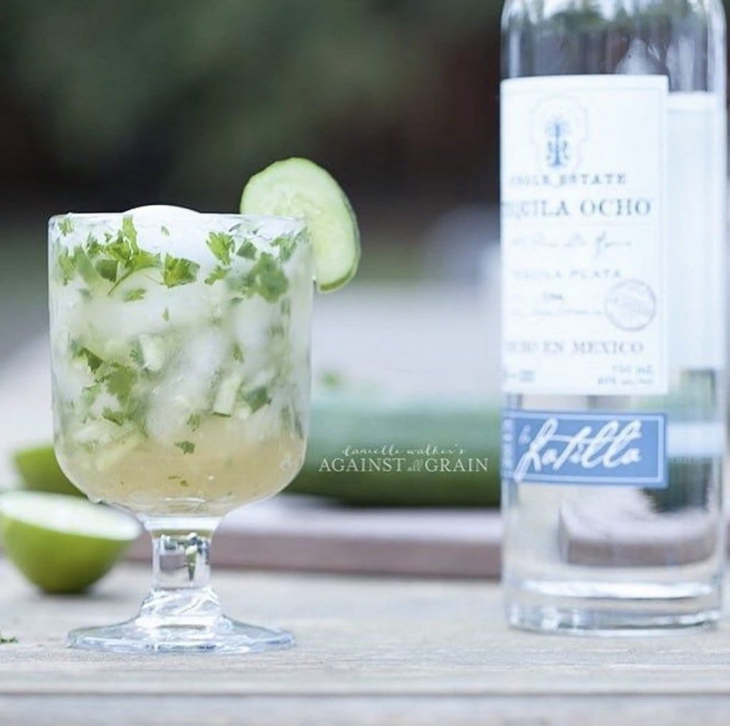A refreshing glass of margarita sit on an outdoor table next to a bottle of tequila