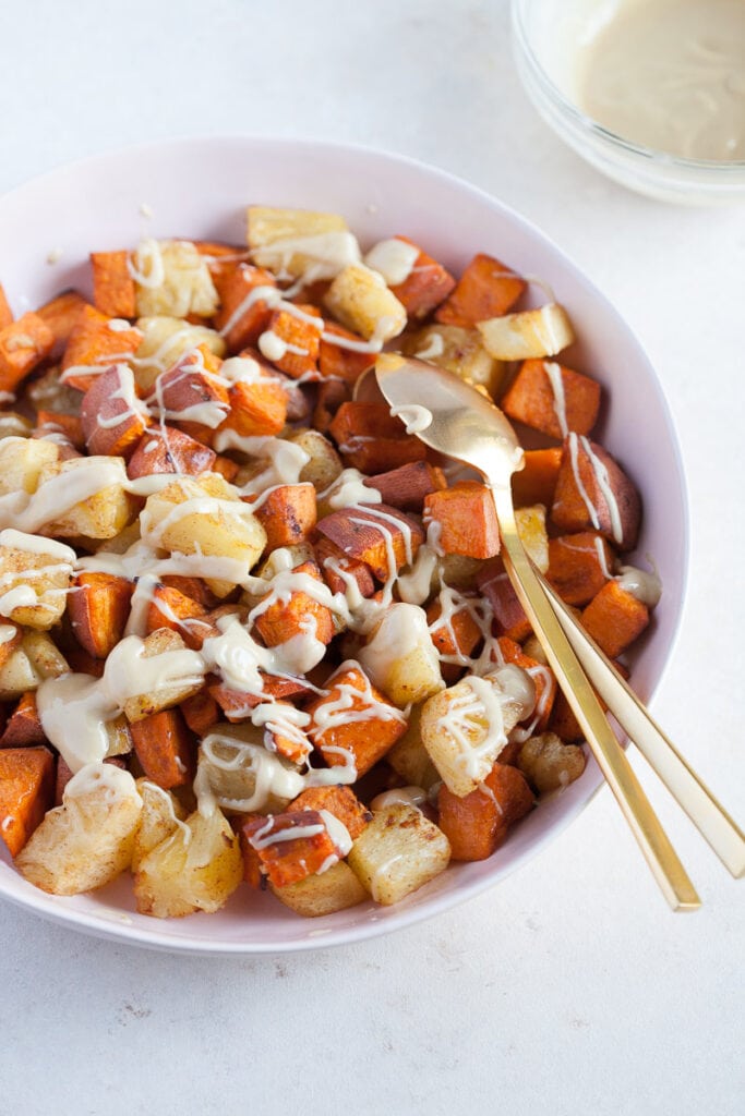 white bowl with gold colored spoon full of Roasted Pineapple and Sweet Potatoes with Cinnamon Cashew drizzle