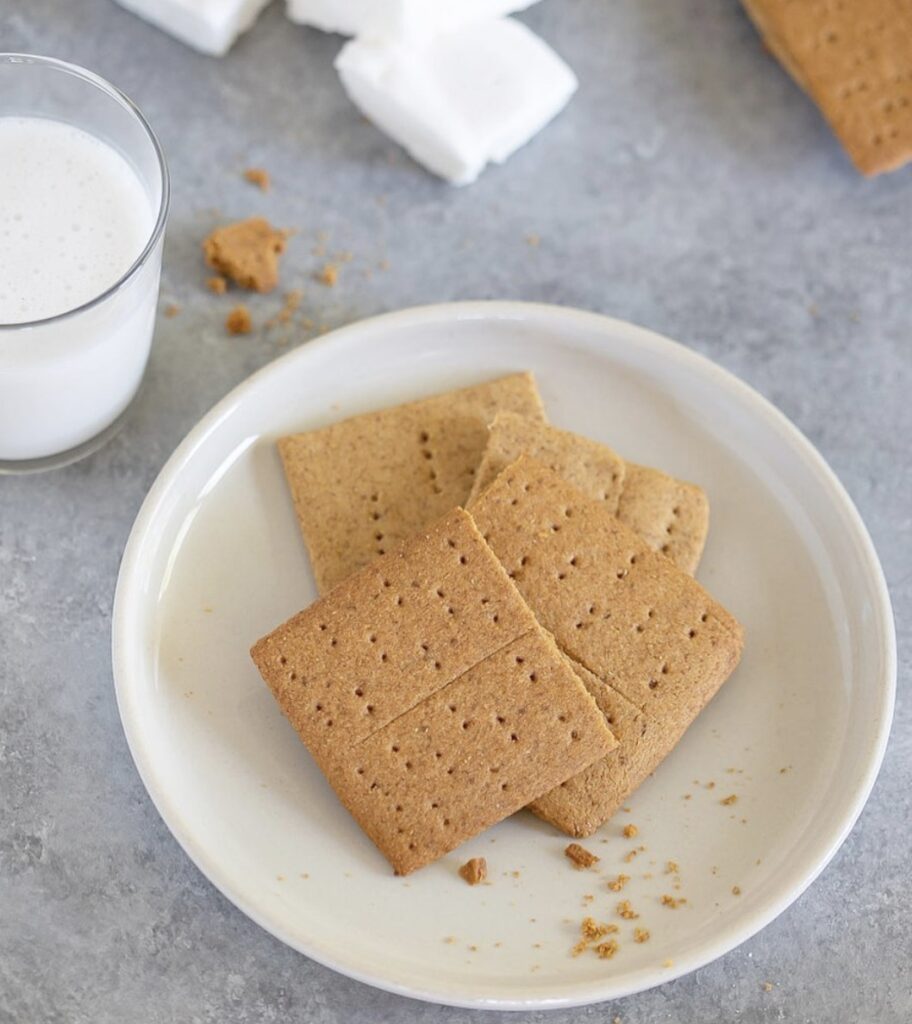 homemade gluten free graham crackers on a white plate next to a glass of milk