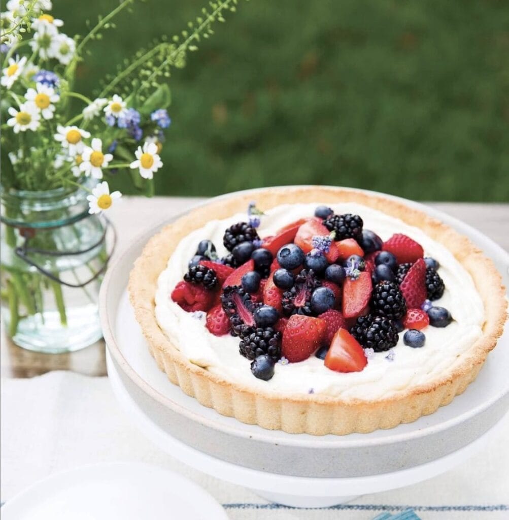 Vanilla Custard tart topped with fresh blueberries, strawberries and raspberries on an outdoor table