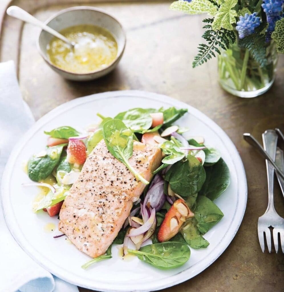 cooked salmon on a bed of fresh greens on white plate set on a wooden table