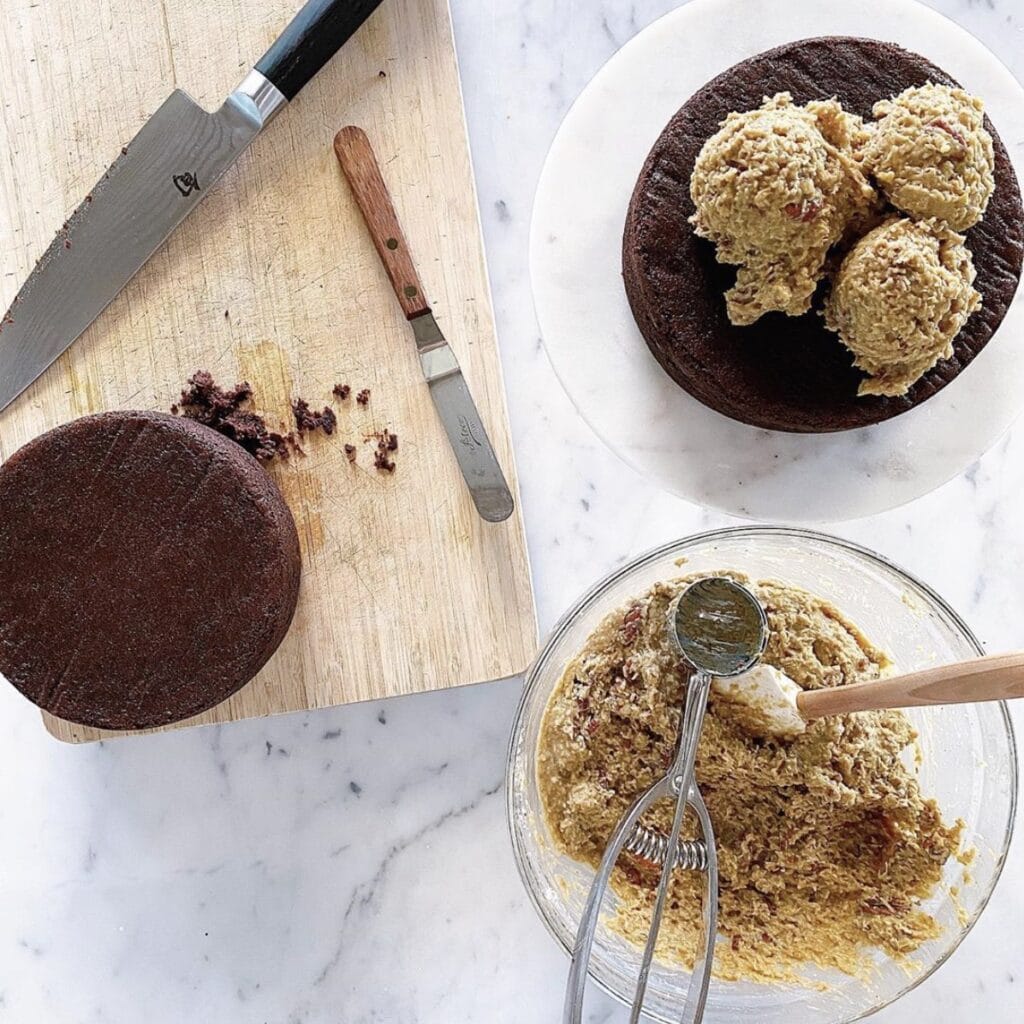 German Chocolate Cake in the process of being made - un-iced chocolate cake on a wooden cutting board and the coconut topping being prepared in a glass bowl